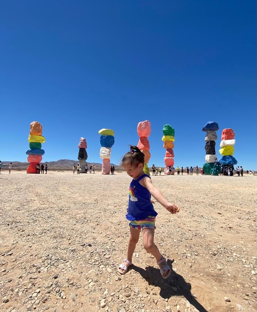 Child walking near colorful rock formations under a clear blue sky in a desert landscape.