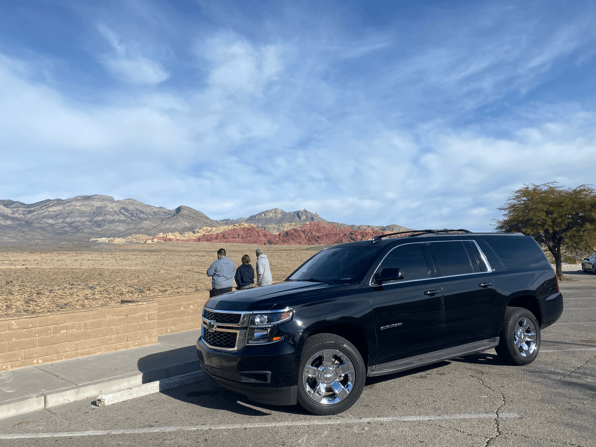 Black SUV parked near people overlooking a desert landscape with mountains in the background.